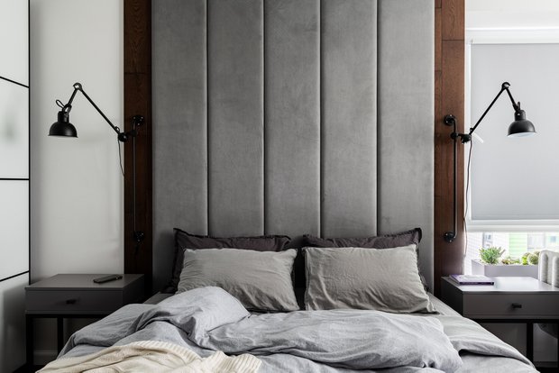 Мягкое изголовье кровати занимает все пространство стены до потолка и обрамлено по бокам паркетными досками с пола.