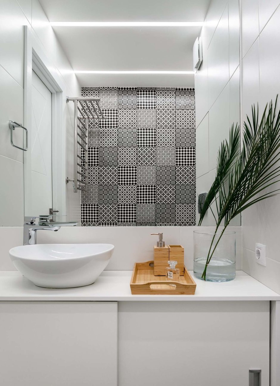 Для акцентной стены в ванной выбрали плитку с черными узорами. Они добавляют графичности монохромному интерьеру. 