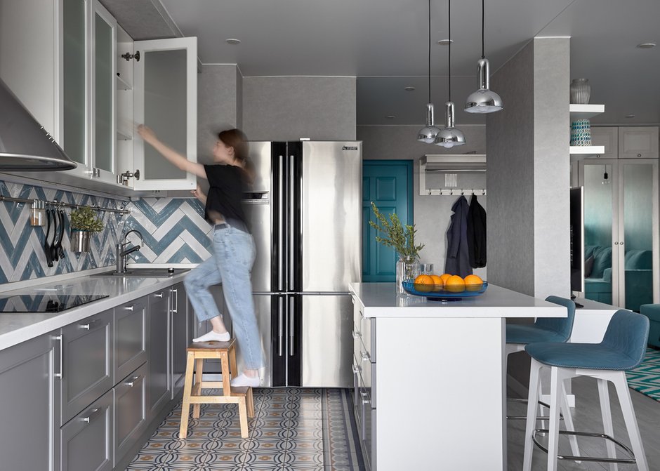 Нижние кухонные фасады выполнены в сером цвете, а верхние — в молочном для того, чтобы визуально сделать пространство кухни более воздушным.